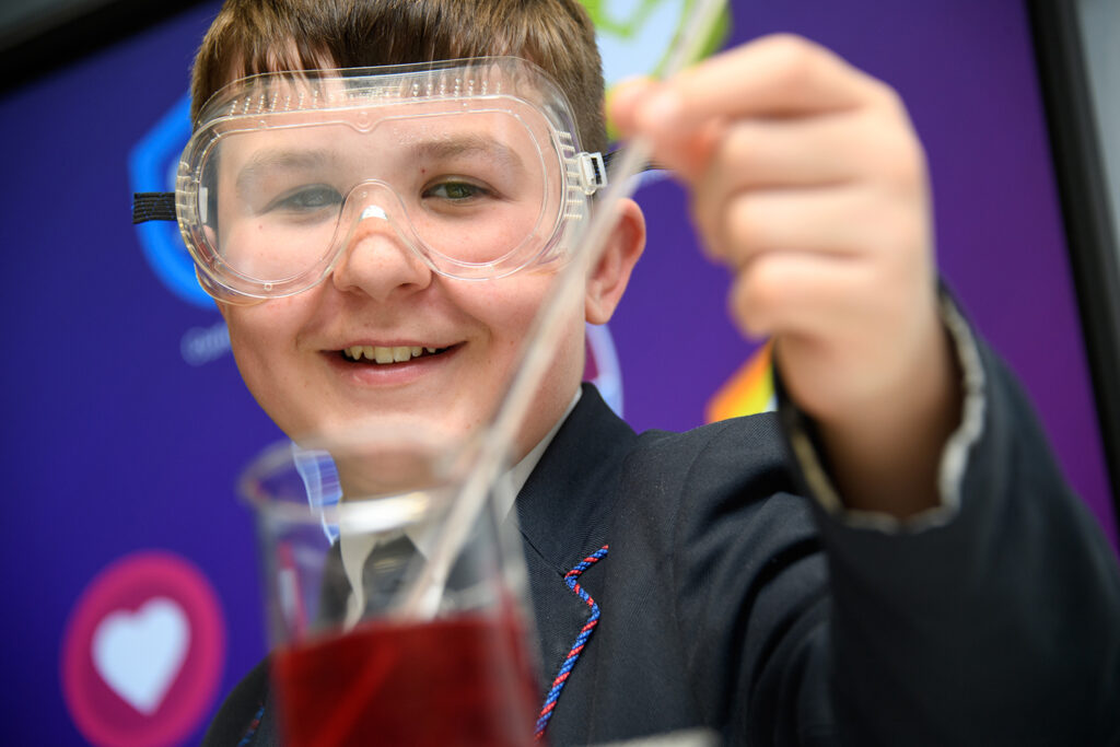 Close up of boy wearing goggles, holding thermometer in a beaker