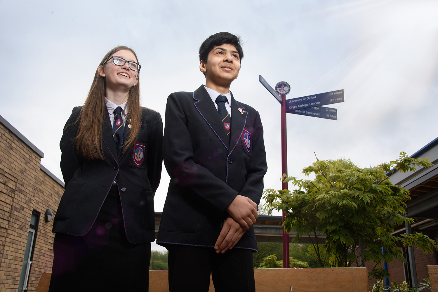 Lower shot of male and female student standing next to school sign looking out into distance