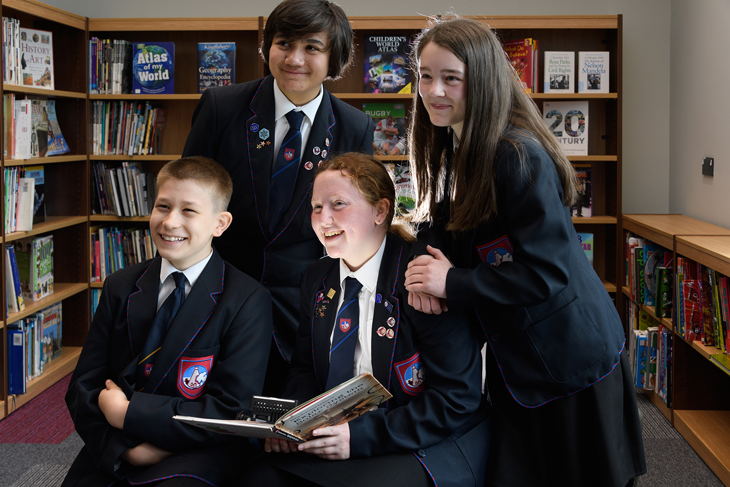Four students in the library, holding a book smiling up
