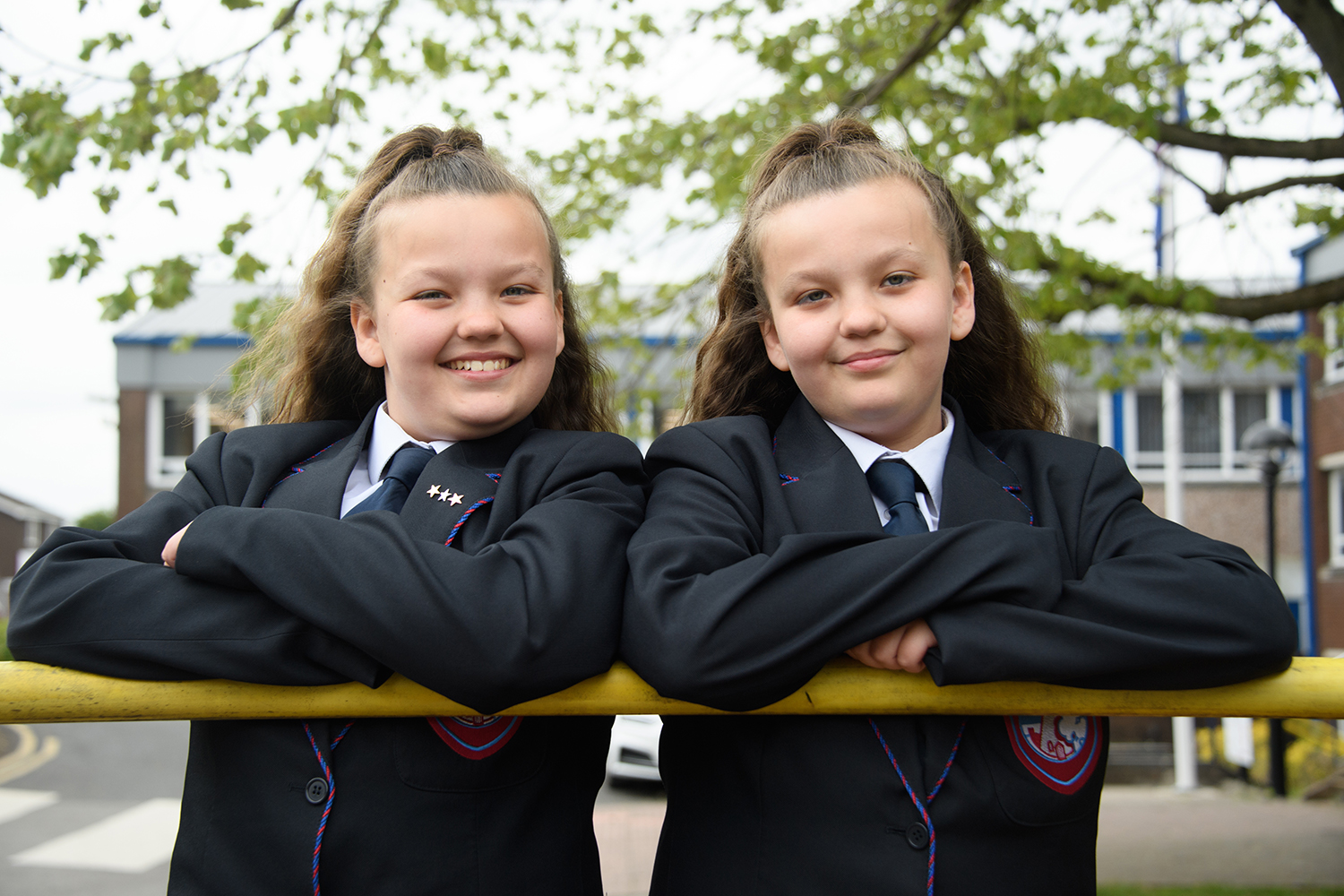 Twin girl students leaning on pole smiling at camera