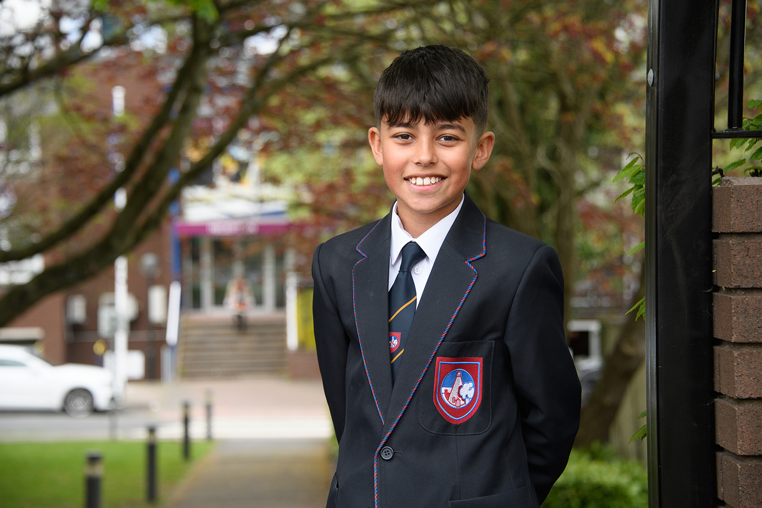Boy student in uniform smiling in front of school entrance