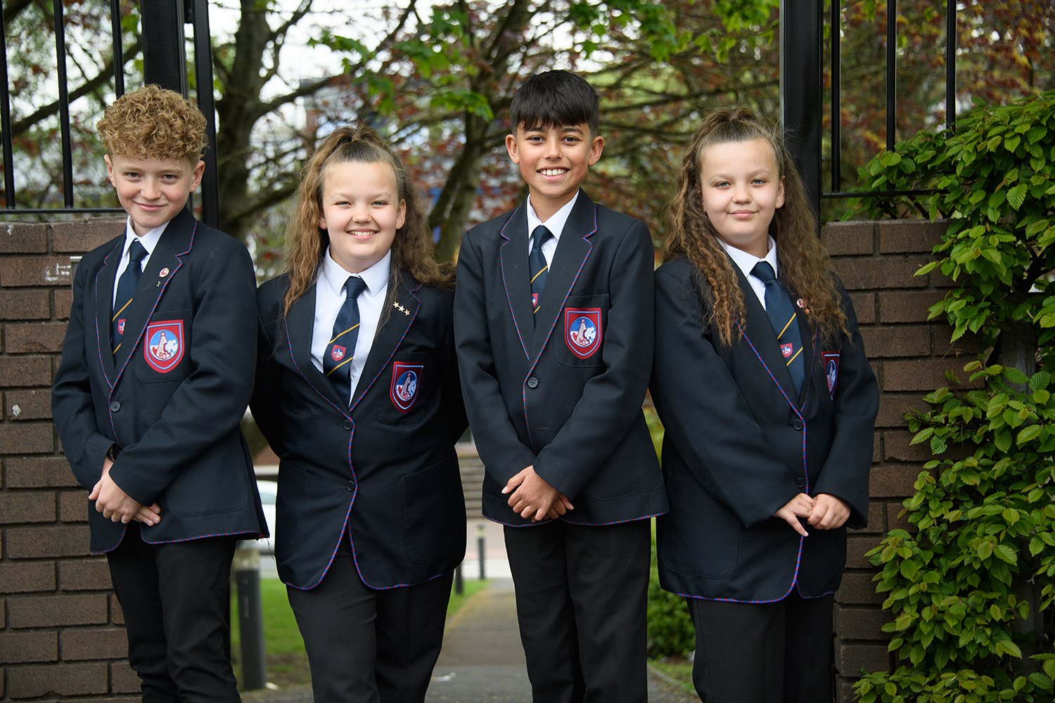 Four students in uniform smiling in front of school entrance