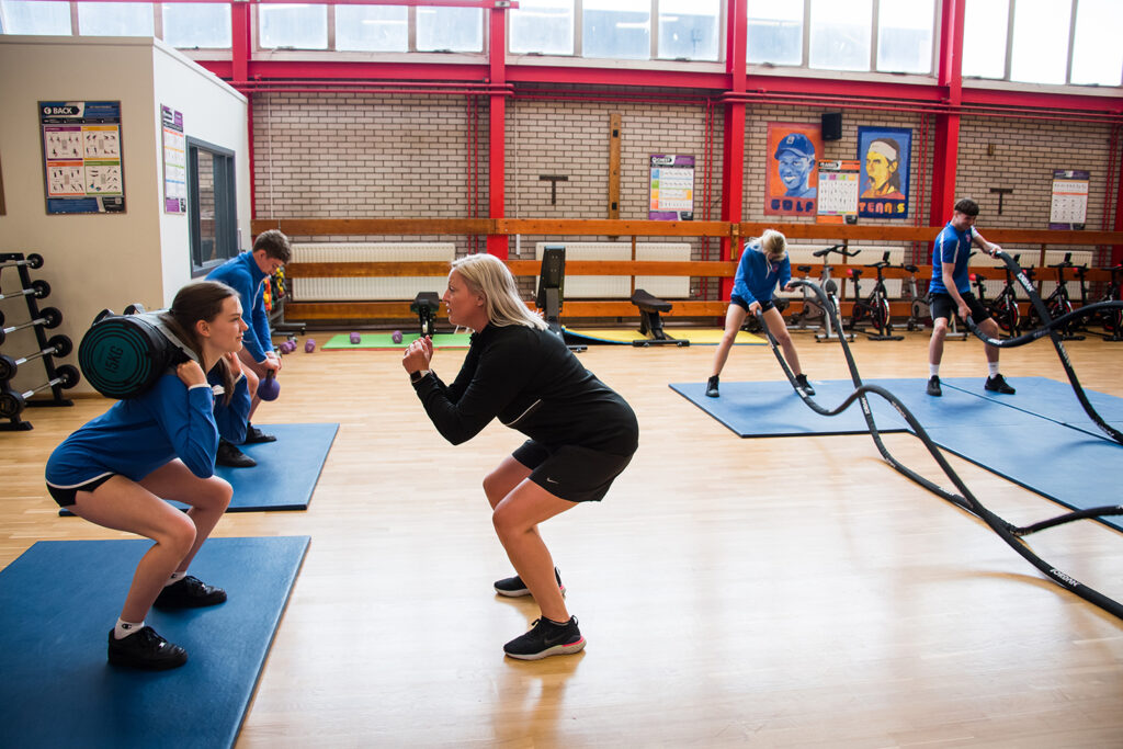 Female PE teacher showing students how to lift weights