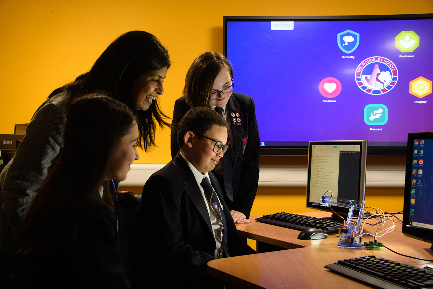 Teacher showing three students how to use small robot in classroom with yellow tint