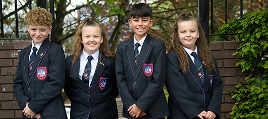 Four students in uniform smiling in front of school entrance