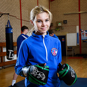 Girl in PE kit and boxing gloves smiling at camera