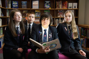 Four students in the library holding an open book together