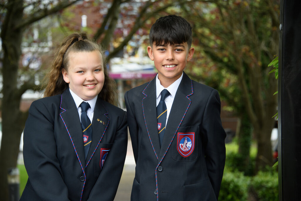 Two students in uniform smiling in front of school entrance