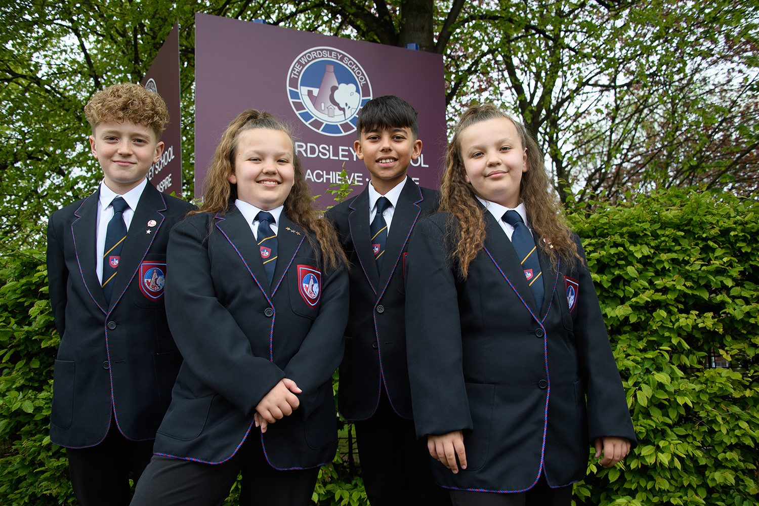 Four students in uniform smiling outside of school entrance