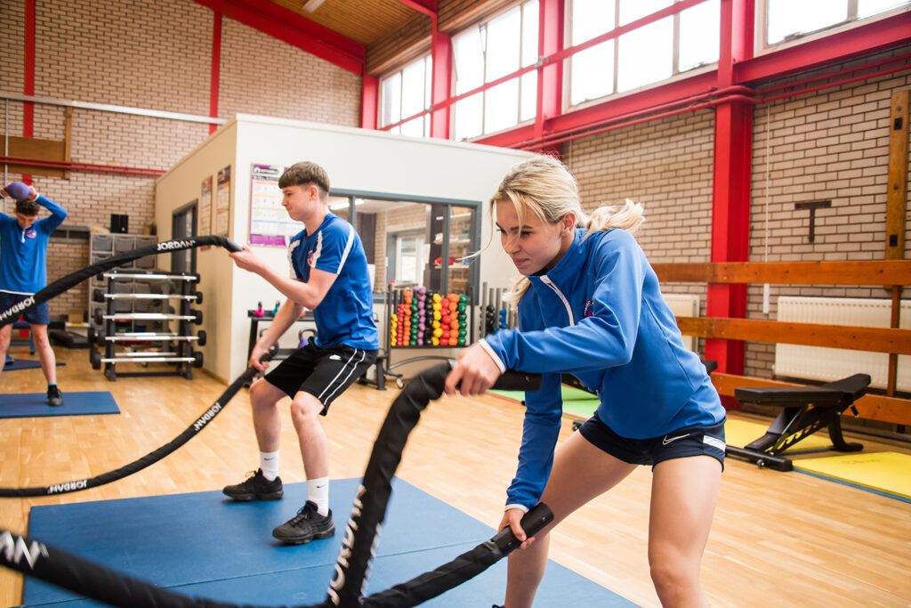 Two students in PE kits using weighted ropes in the gym